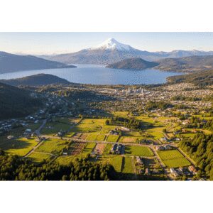 Vista aérea panorámica de la ciudad de Villarrica, el Lago Villarrica y el Volcán Villarrica nevado al fondo, mostrando áreas verdes y diversas parcelas en los alrededores, simbolizando la belleza natural y las oportunidades de inversión inmobiliaria en la región.